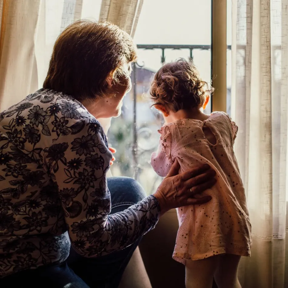 A carer and child looking out of a sunlit window at home in Cyprus